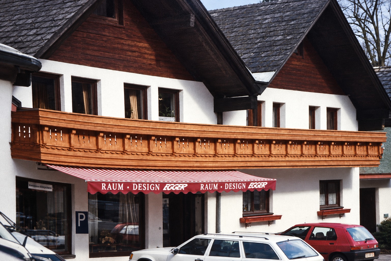 Historische Außenansicht des Egger-Geschäfts mit Holzbalkon und roter Markise