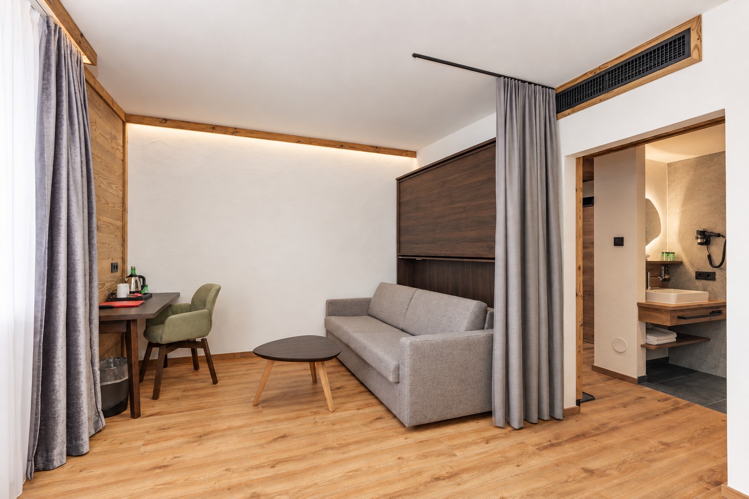 Wohn- und Schlafbereich mit grauem Sofa und flexibler Vorhangtrennung