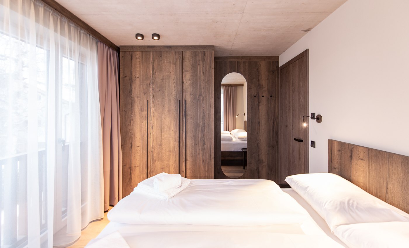 Schlafzimmer mit Holzwand, Doppelbett und hellen Vorhängen